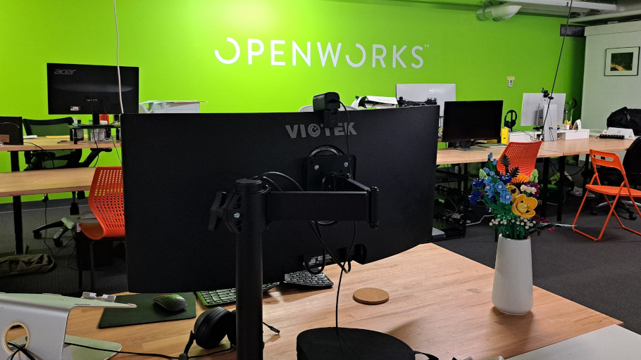 Dedicated full-time member desk with monitors set against green wall with OpenWorks logo.